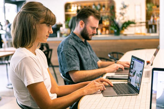 Two young professional freelance website designer working on laptops in a modern cafe setting.